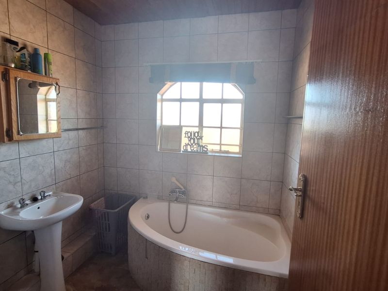 A functional bathroom featuring a corner bathtub, pedestal basin, and wall-mounted medicine cabinet with tiled finishes throughout.