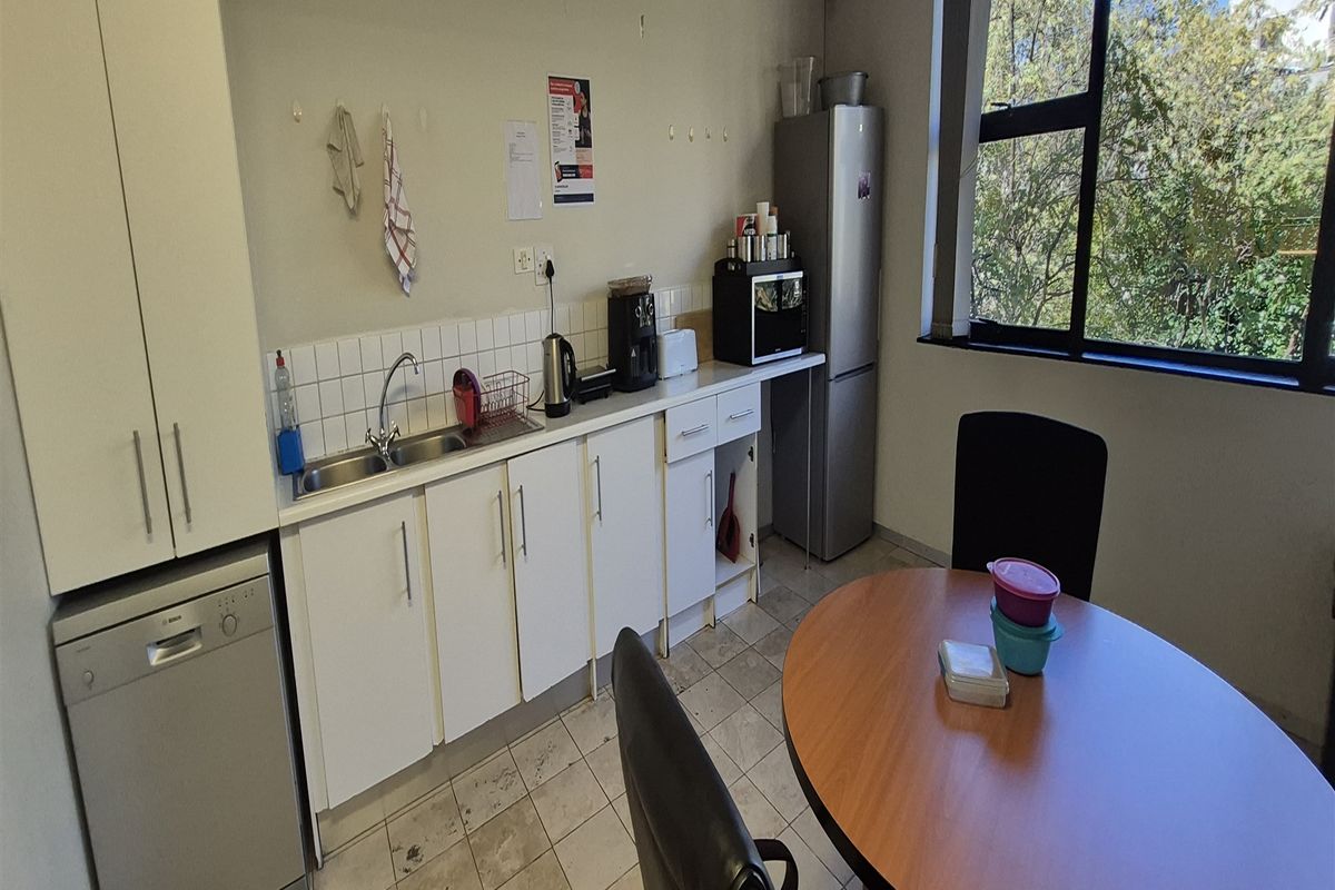 A functional office kitchenette featuring white cabinetry, a stainless steel sink, tiled backsplash, and large windows providing natural light.