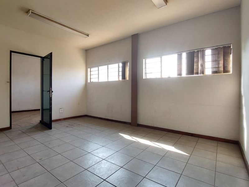 An empty office space featuring tiled flooring, horizontal windows, and fluorescent lighting, requiring minor cosmetic updates to improve its overall presentation.