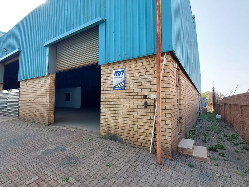 Industrial warehouse exterior featuring a large roller shutter door, blue corrugated metal cladding, and face brick facade with paved access area.
