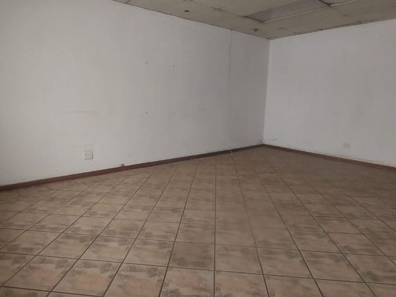 An empty office space featuring tiled flooring, a drop ceiling, and a glass panel door, suitable for commercial or industrial use.