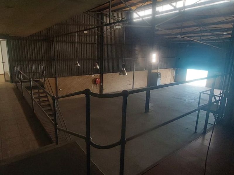 Spacious industrial open-plan warehouse area featuring a mezzanine level, exposed steel roof trusses, and concrete flooring, suitable for various commercial or storage applications.