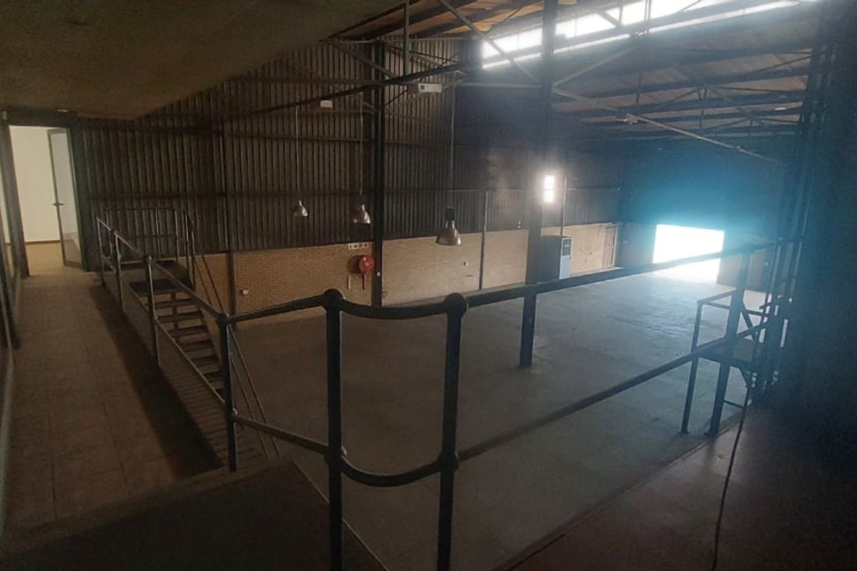 Spacious industrial open-plan warehouse area featuring a mezzanine level, exposed steel roof trusses, and concrete flooring, suitable for various commercial or storage applications.