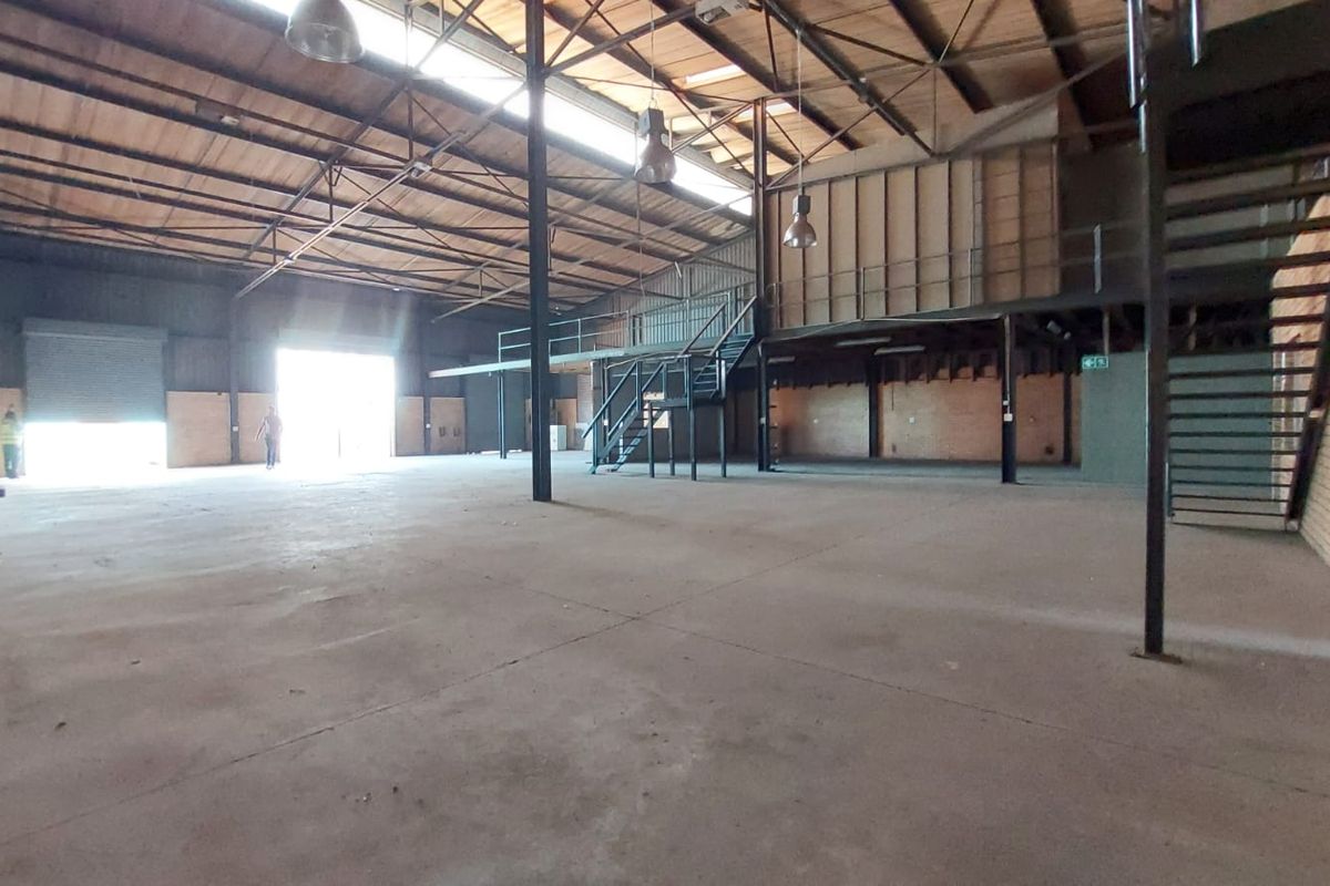 Spacious industrial open-plan warehouse featuring high ceilings with exposed steel trusses, a mezzanine level, concrete flooring, and a large roller shutter door.