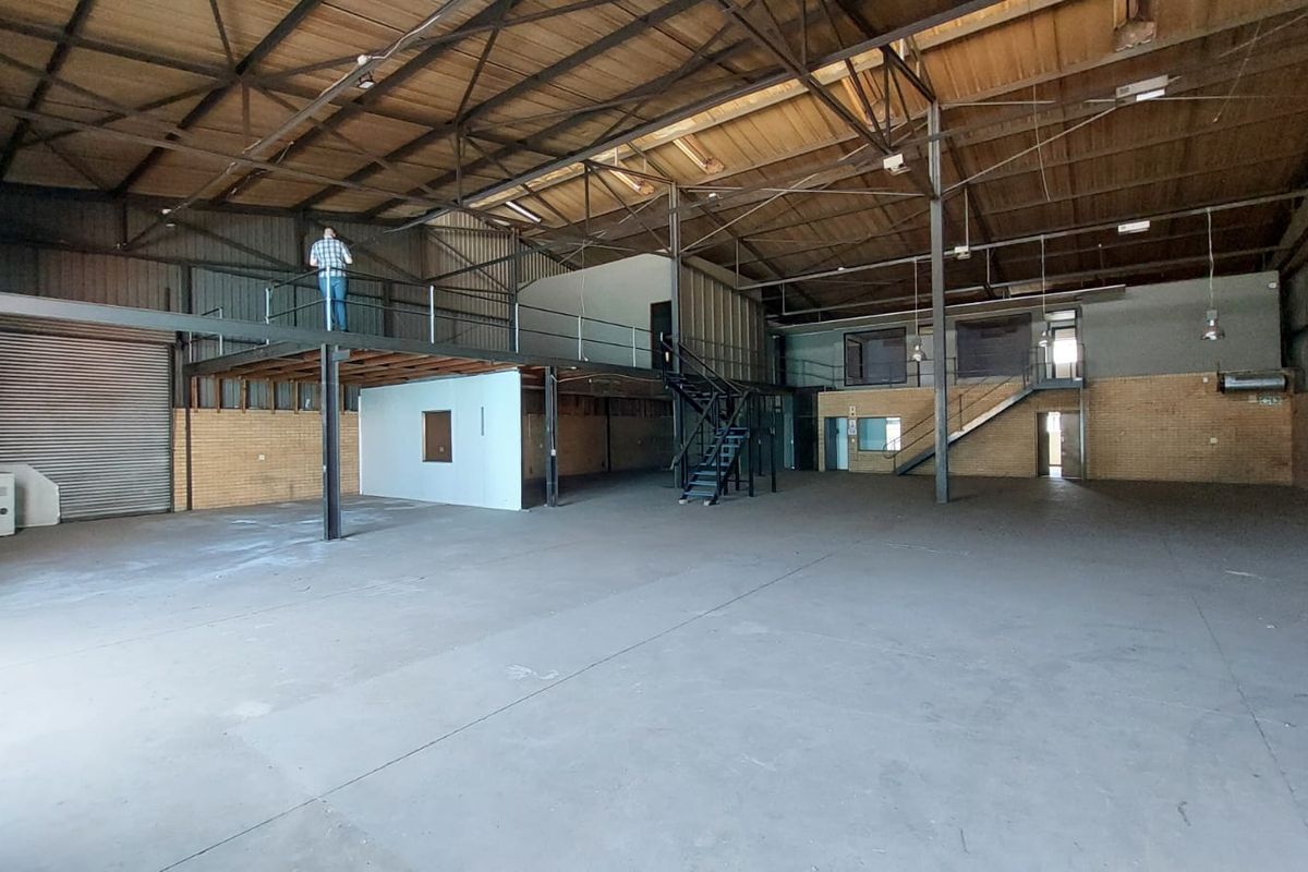 Spacious industrial warehouse featuring a steel mezzanine level, concrete flooring, exposed roof trusses, and a large roller shutter door for easy access.