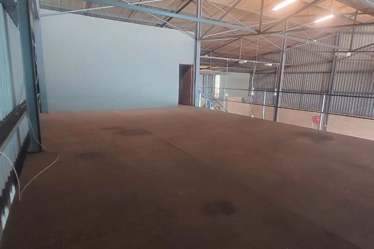 An open-plan mezzanine level within an industrial warehouse, featuring exposed steel roof trusses, metal wall cladding, and a safety railing.