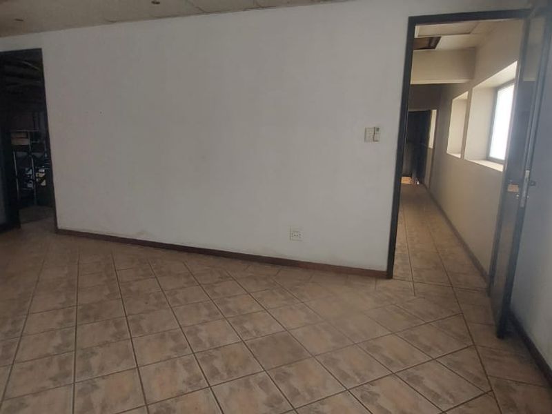 An empty office space featuring tiled flooring, recessed lighting, and access to an adjacent hallway, requiring cosmetic updates to improve its professional appeal.