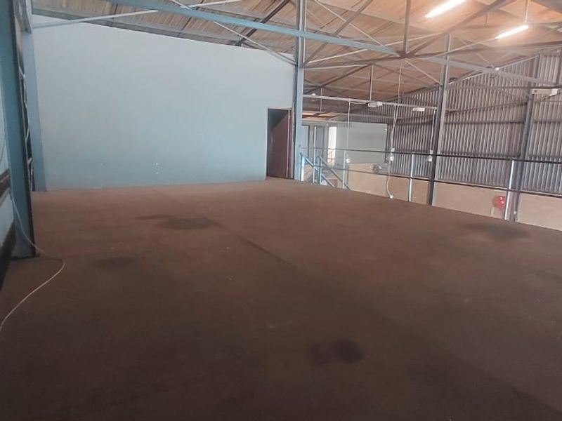 An open-plan mezzanine level within an industrial warehouse, featuring exposed steel roof trusses, metal wall cladding, and a safety railing.