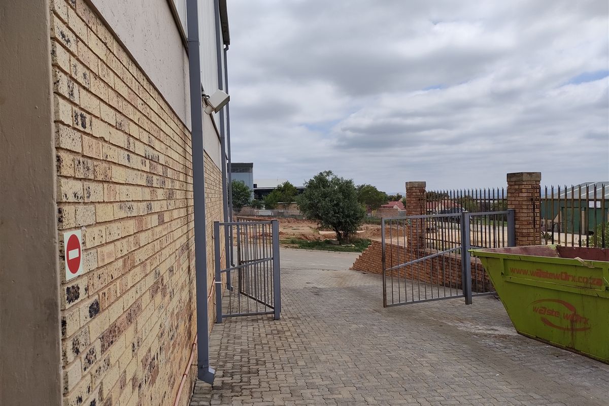Exterior view of the industrial property showing a paved driveway, metal security gates, and brick perimeter walling.