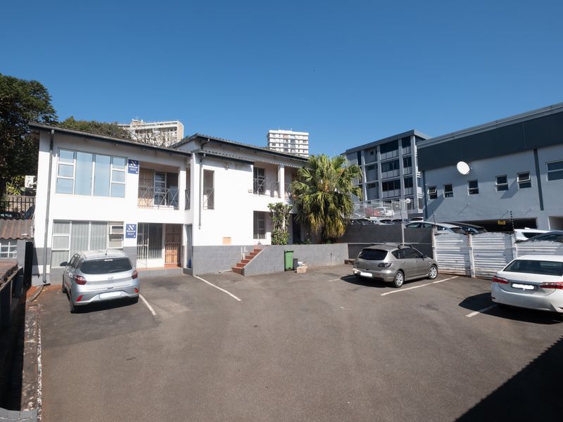 Rear exterior view of the office building featuring a paved parking area, security fencing, and access to upper-level balconies.