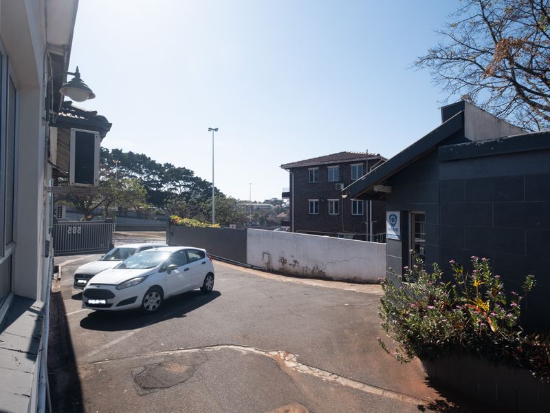 Rear exterior view of the office property featuring an asphalt driveway, perimeter boundary wall, and security access gate.