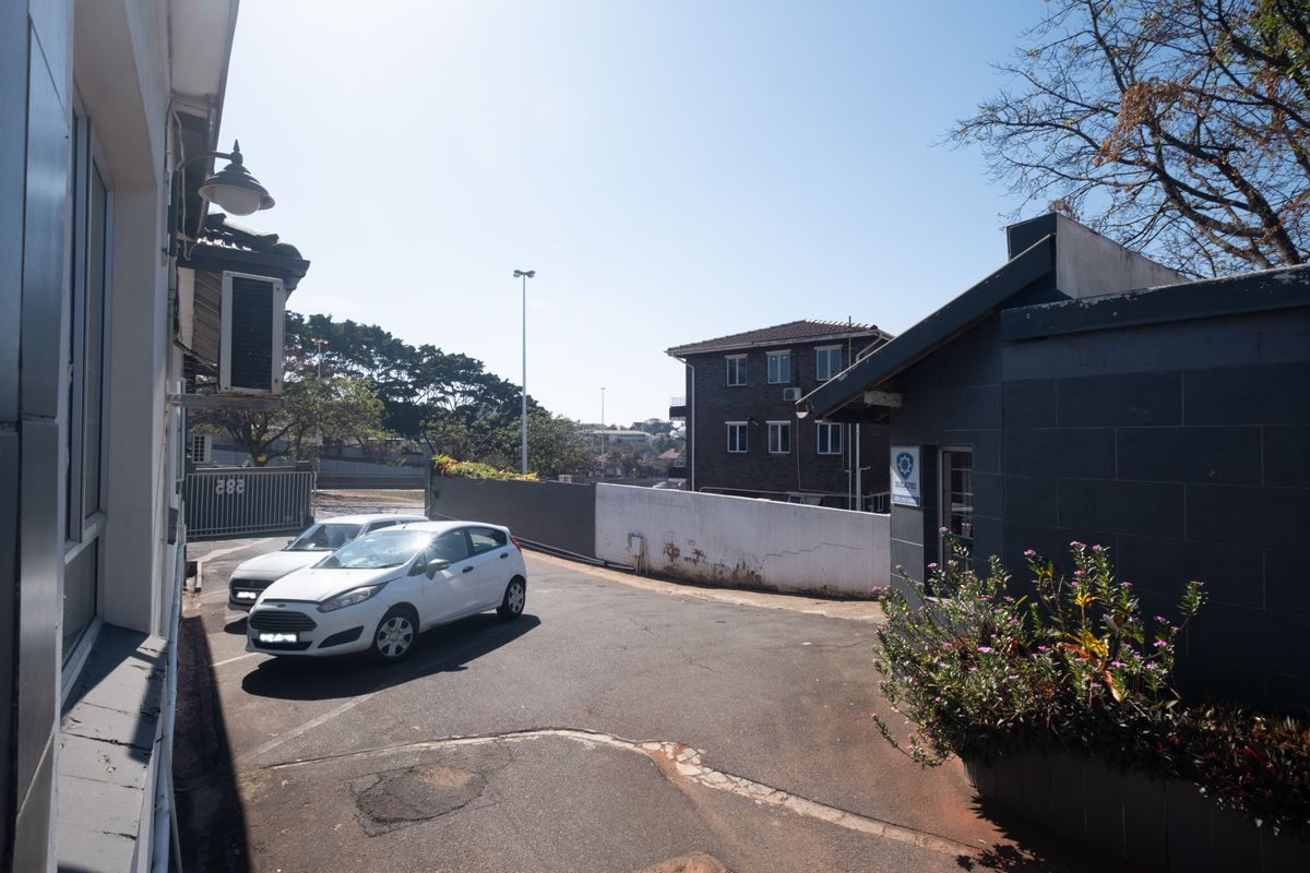 Rear exterior view of the office property featuring an asphalt driveway, perimeter boundary wall, and security access gate.