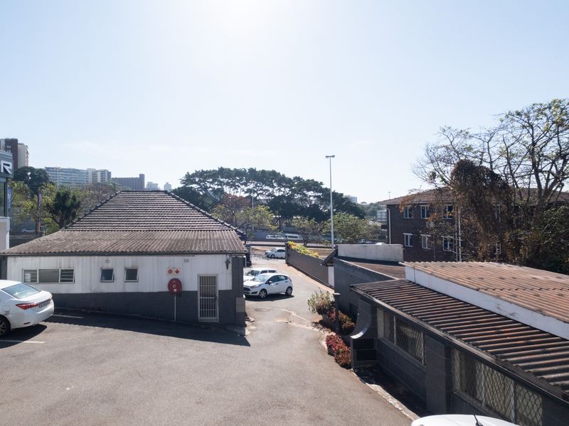 Elevated view of the office property exterior, featuring a paved driveway, tiled roof structures, and surrounding commercial building infrastructure.