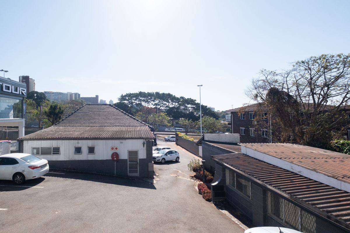 Elevated view of the office property exterior, featuring a paved driveway, tiled roof structures, and surrounding commercial building infrastructure.