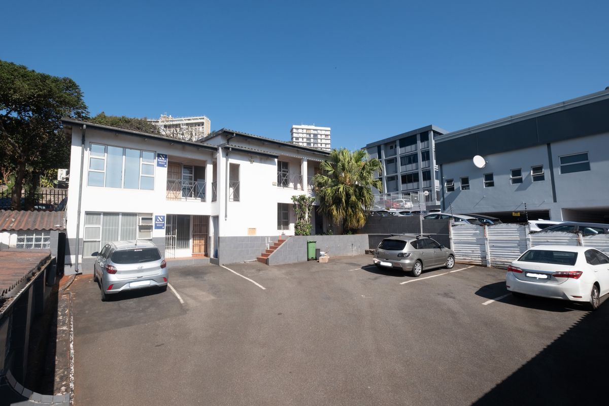 Rear exterior view of the office building featuring a paved parking area, security fencing, and access to upper-level balconies.