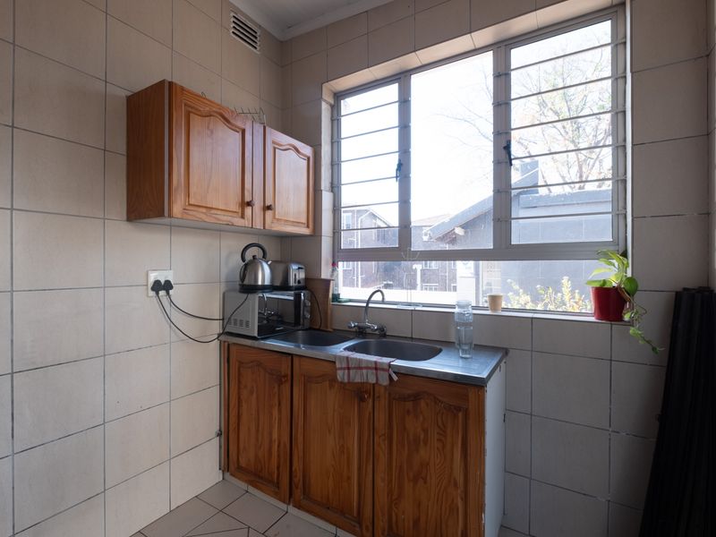 A functional scullery area featuring tiled walls, wooden cabinetry, and a stainless steel sink with a window providing natural light.