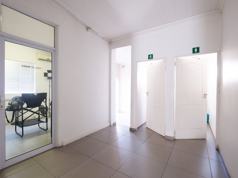 A clean, well-lit office hallway featuring tiled flooring, a glass partition door, and access to separate male and female restroom facilities.