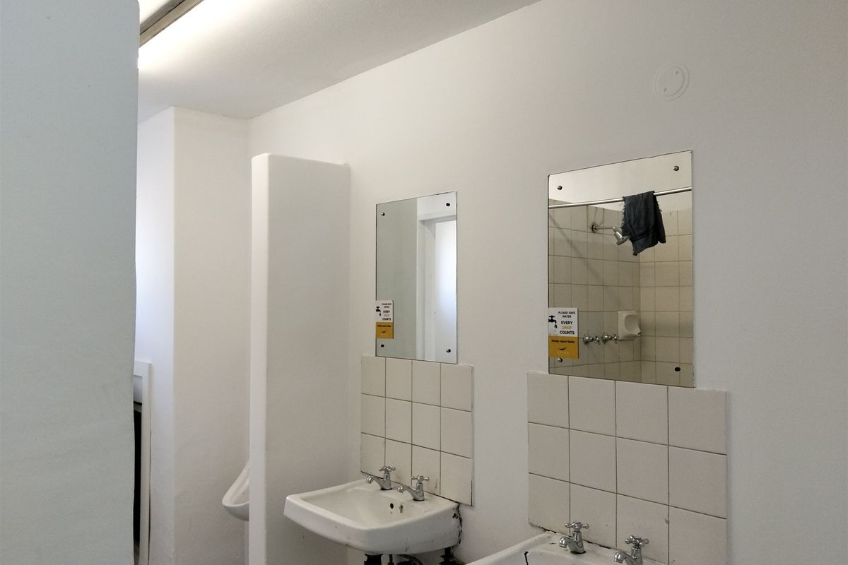 Functional industrial-style communal bathroom featuring dual wall-mounted ceramic basins, tiled splashbacks, and wall-mounted mirrors.