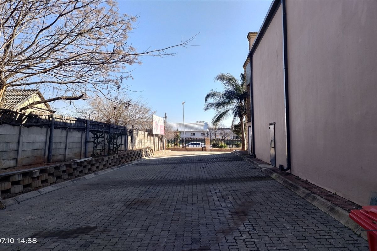Exterior view of the industrial property showing a paved driveway area alongside the building structure with perimeter walling.
