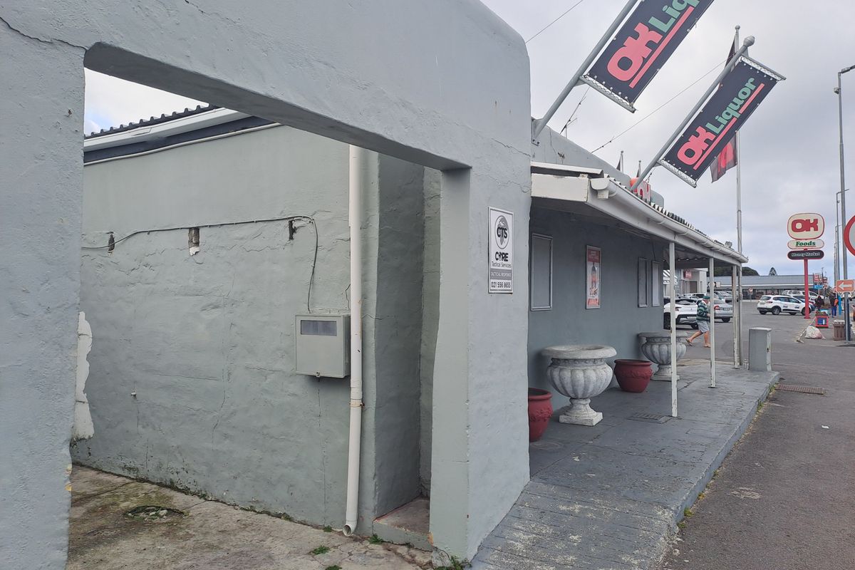 Front exterior view of a commercial retail building featuring a covered walkway, concrete ramp access, and prominent signage for an OK Liquor store.