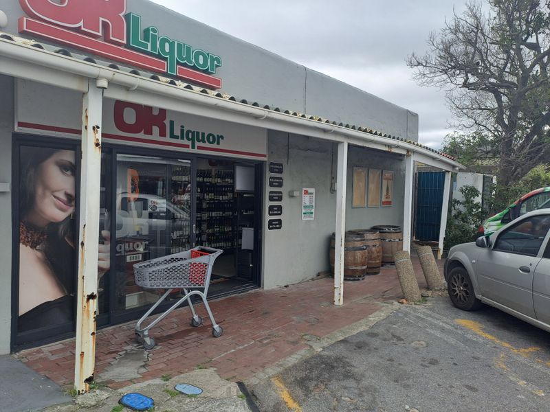 Front facade of a commercial liquor store featuring a covered walkway, sliding glass entrance, and brick paved exterior area.