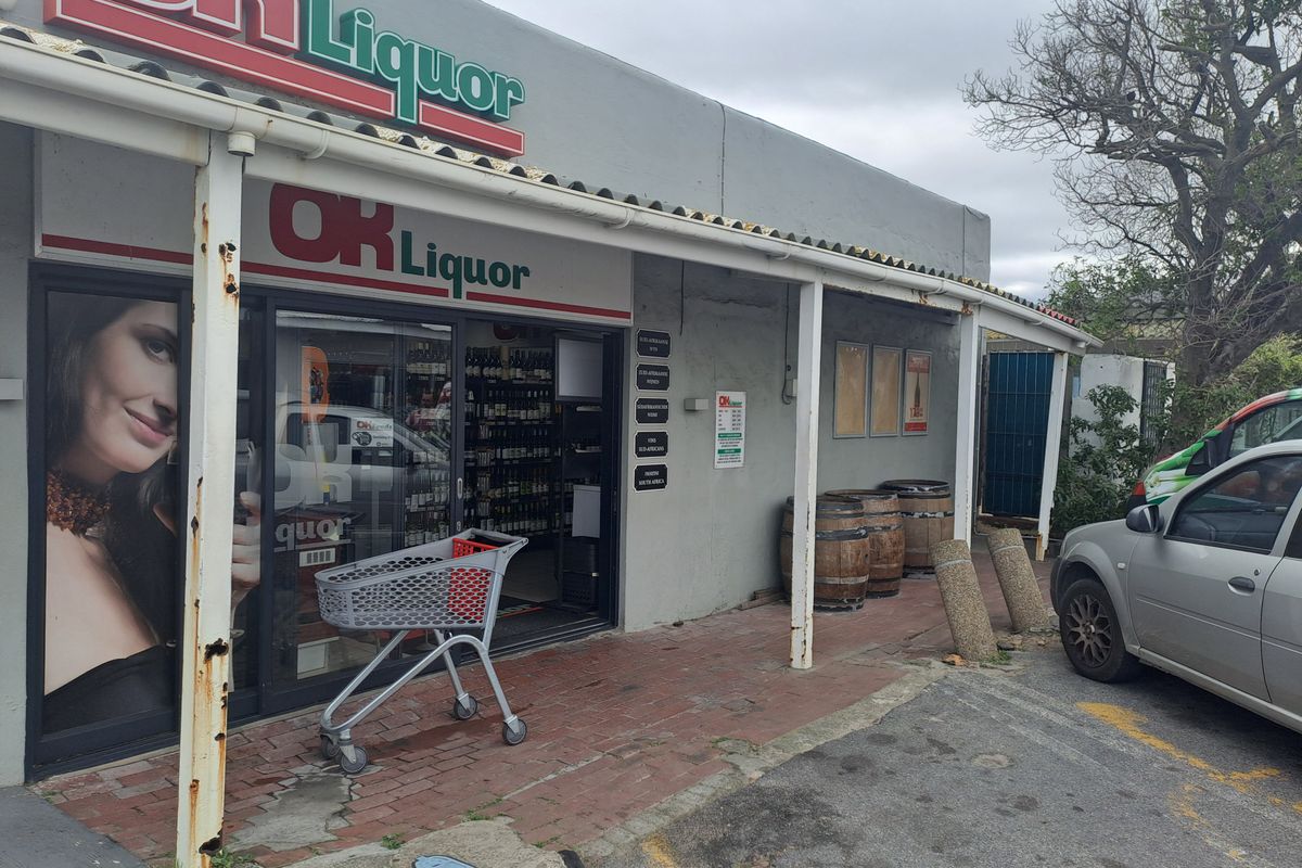 Front facade of a commercial liquor store featuring a covered walkway, sliding glass entrance, and brick paved exterior area.