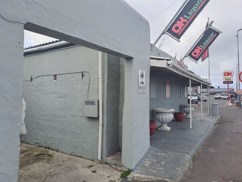 Front exterior view of a commercial retail building featuring a covered walkway, concrete ramp access, and prominent signage for an OK Liquor store.