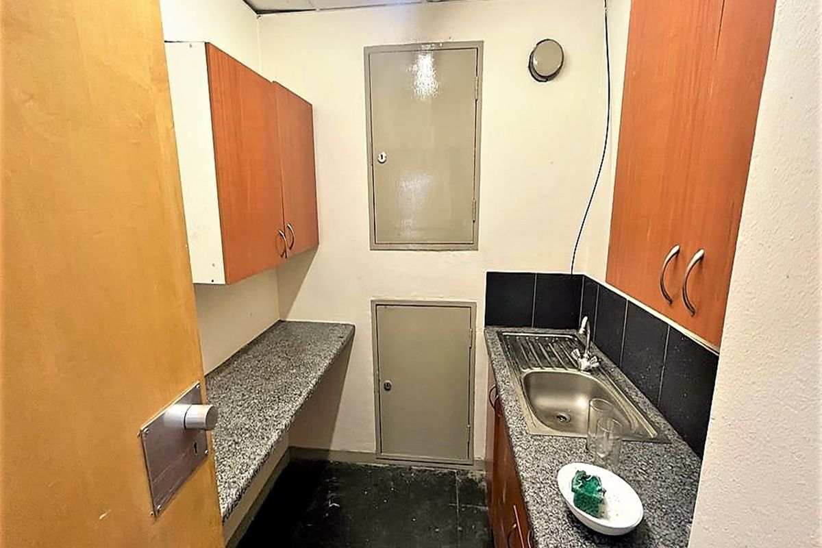 A compact office kitchenette featuring laminate countertops, stainless steel sink, and built-in wooden cabinetry with overhead storage.
