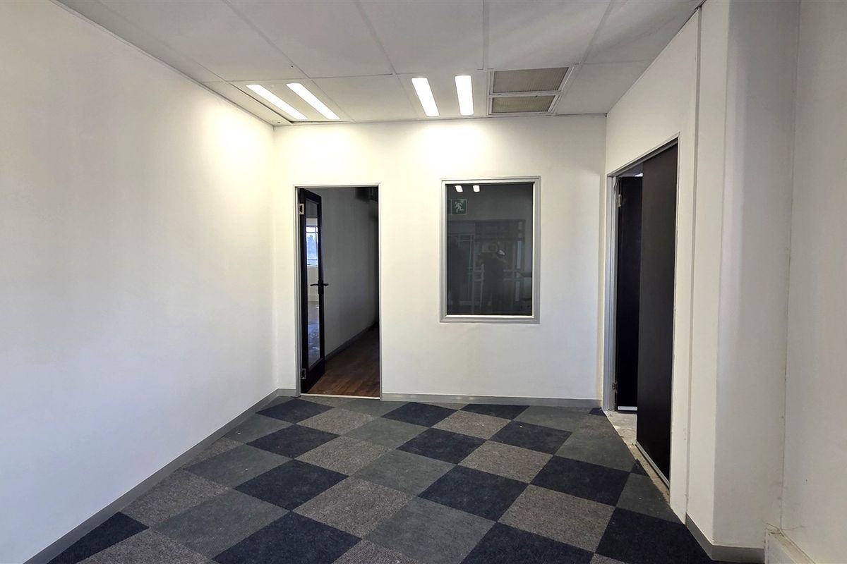 A clean, empty office space featuring carpet tiles, recessed ceiling lighting, and an internal window, providing a functional and professional work environment.