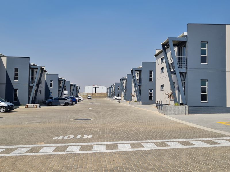 A view of a modern industrial park featuring multiple warehouse units with integrated office spaces and a paved central driveway.