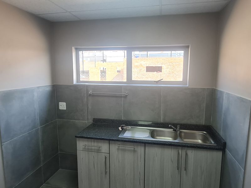 A clean and functional scullery area featuring a double bowl stainless steel sink, granite countertops, and modern grey cabinetry with tiled splashbacks.