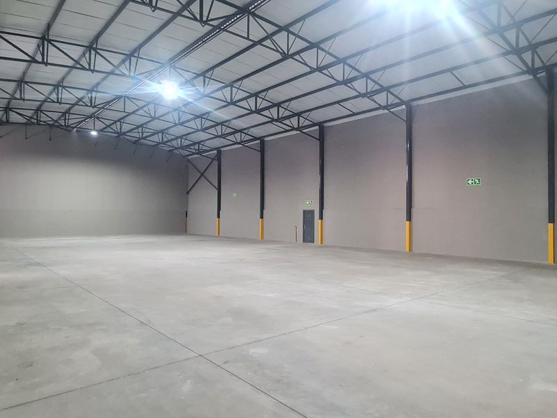 Spacious industrial warehouse unit featuring high ceilings with exposed steel trusses, polished concrete flooring, and integrated fire safety equipment.