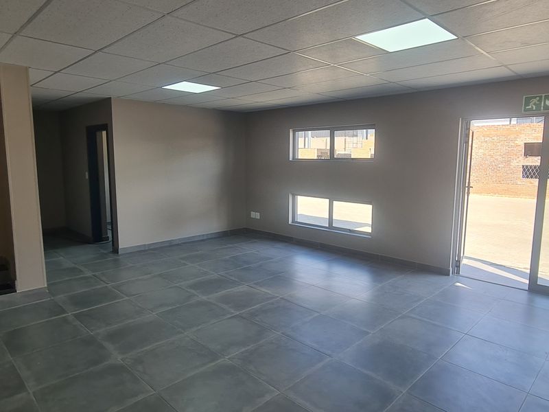Spacious open-plan industrial office area featuring tiled flooring, a suspended ceiling with recessed lighting, and direct access to an exterior paved yard.