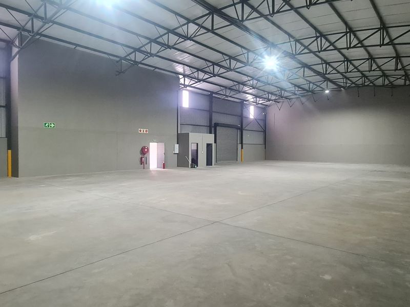 A spacious, clean industrial warehouse unit featuring high ceilings with exposed steel trusses, polished concrete flooring, and a large roller shutter door.