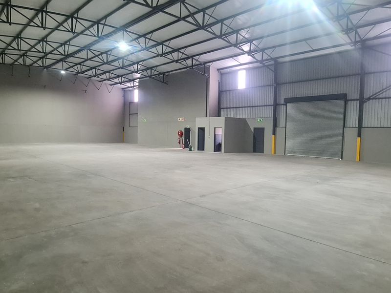 Spacious industrial warehouse unit featuring high ceilings with exposed steel trusses, polished concrete flooring, and a large roller shutter door for easy access.