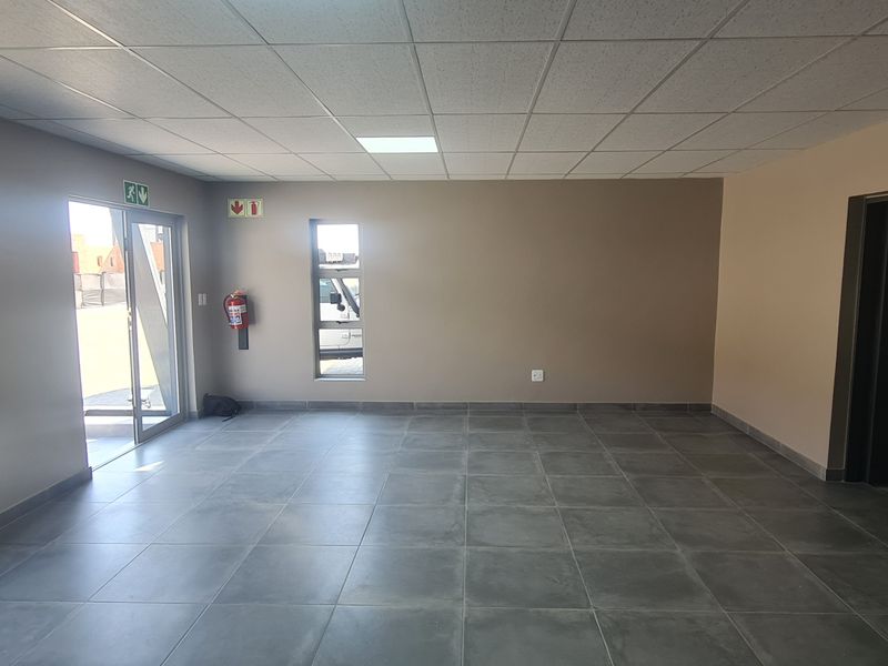 A clean, vacant industrial office space featuring modern grey floor tiles, a suspended ceiling, and natural light from multiple windows.
