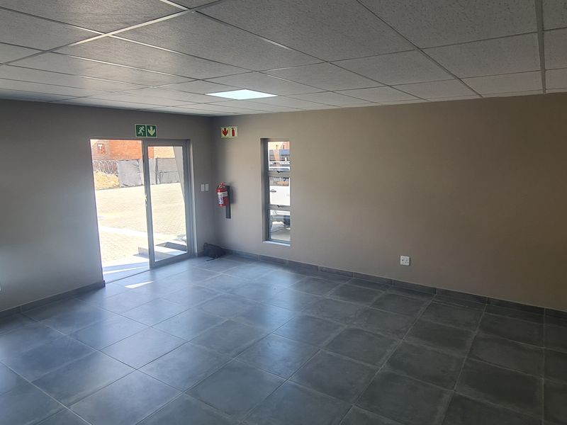 A clean, modern, and empty office space featuring tiled flooring, a suspended ceiling with recessed lighting, and natural light from multiple windows.