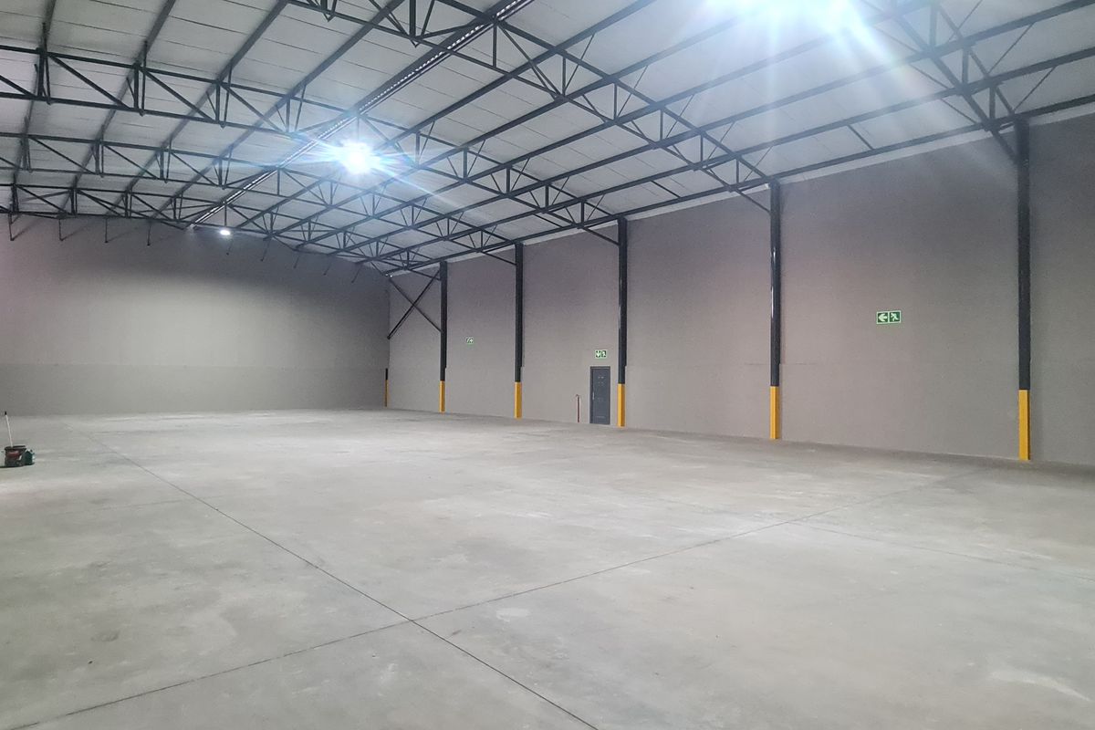 Spacious industrial warehouse unit featuring high ceilings with exposed steel trusses, polished concrete flooring, and integrated fire safety equipment.