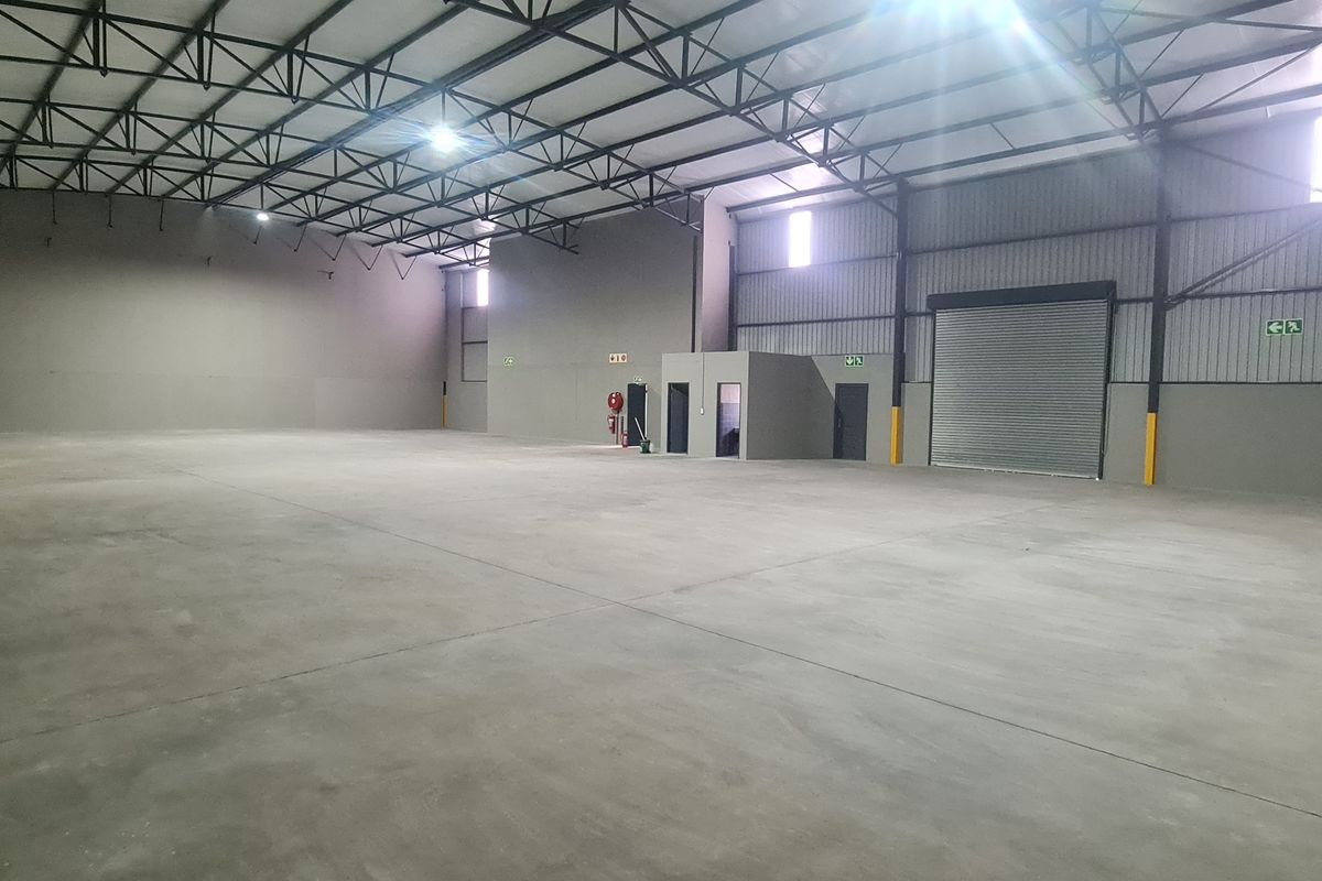 Spacious industrial warehouse unit featuring high ceilings with exposed steel trusses, polished concrete flooring, and a large roller shutter door for easy access.