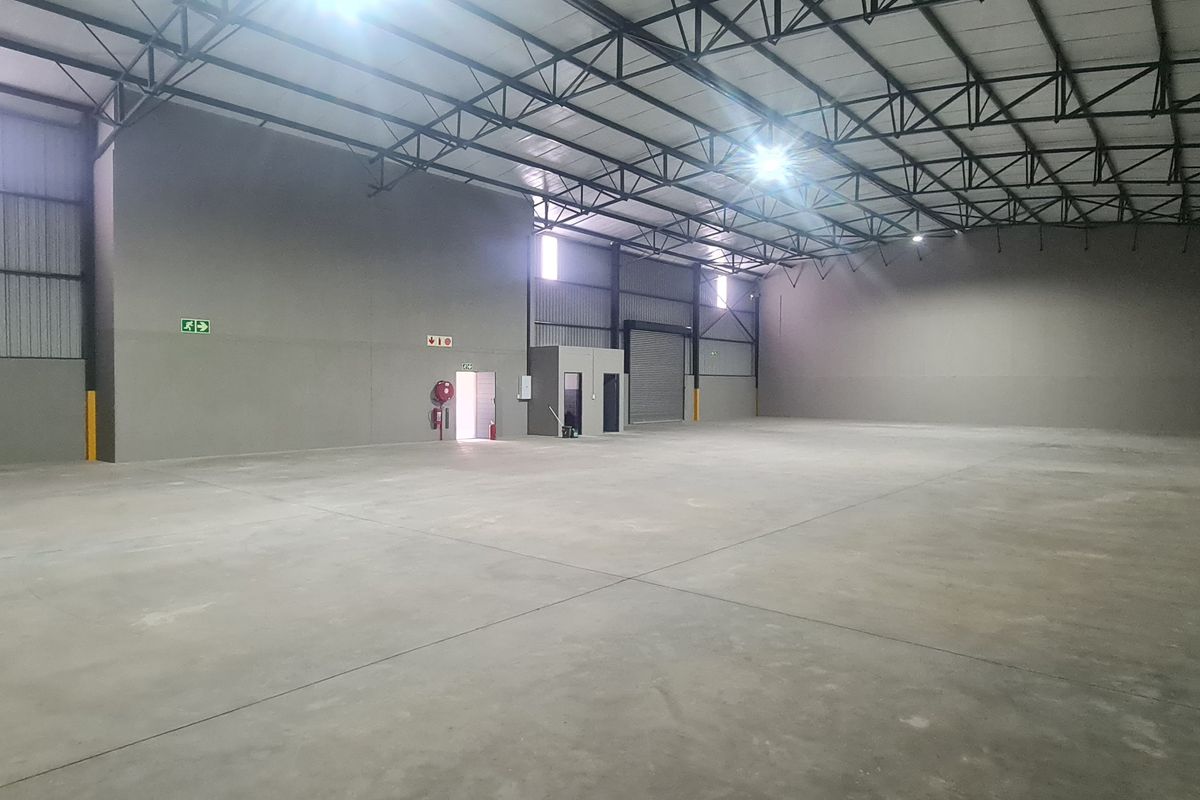A spacious, clean industrial warehouse unit featuring high ceilings with exposed steel trusses, polished concrete flooring, and a large roller shutter door.