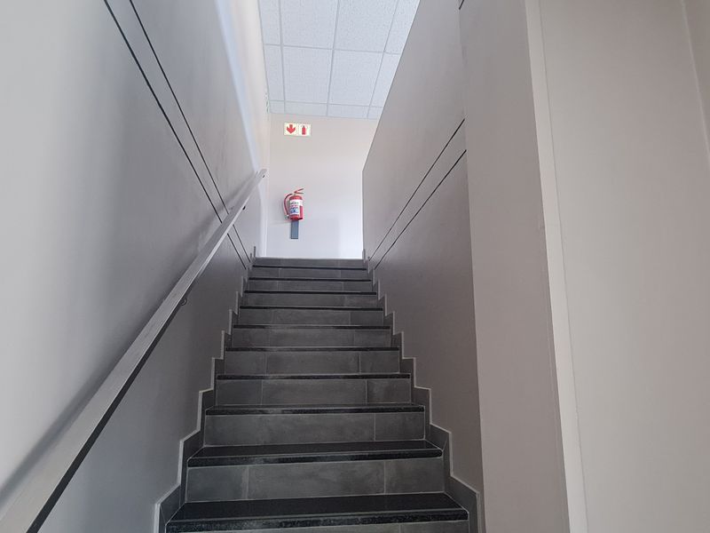 A clean, modern industrial staircase featuring tiled steps, a wall-mounted handrail, and a fire safety installation.