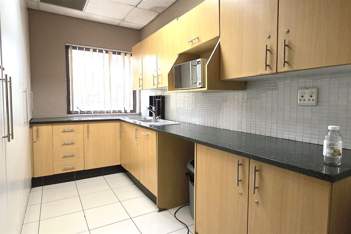 A functional office kitchenette featuring light wood cabinetry, dark granite countertops, a stainless steel sink, and tiled flooring.