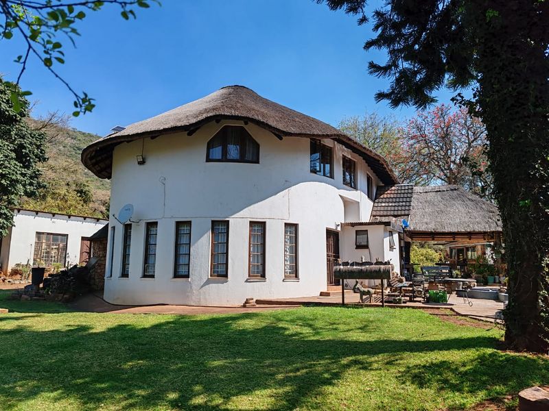 Rear view of a circular farmhouse featuring a traditional thatch roof, timber-framed windows, and an adjoining paved patio area set within a garden.