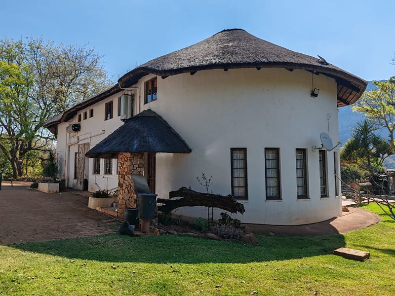 Rear view of a farm-style dwelling featuring a traditional thatch roof, stone-clad entrance detail, and surrounding landscaped garden area.