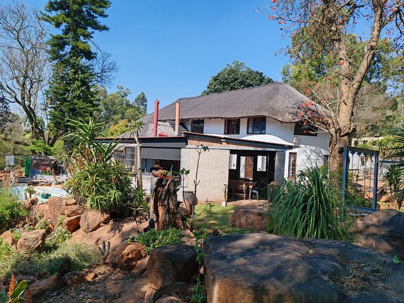 Rear view of a traditional thatched-roof farmhouse featuring a covered patio area and established rock garden landscaping.