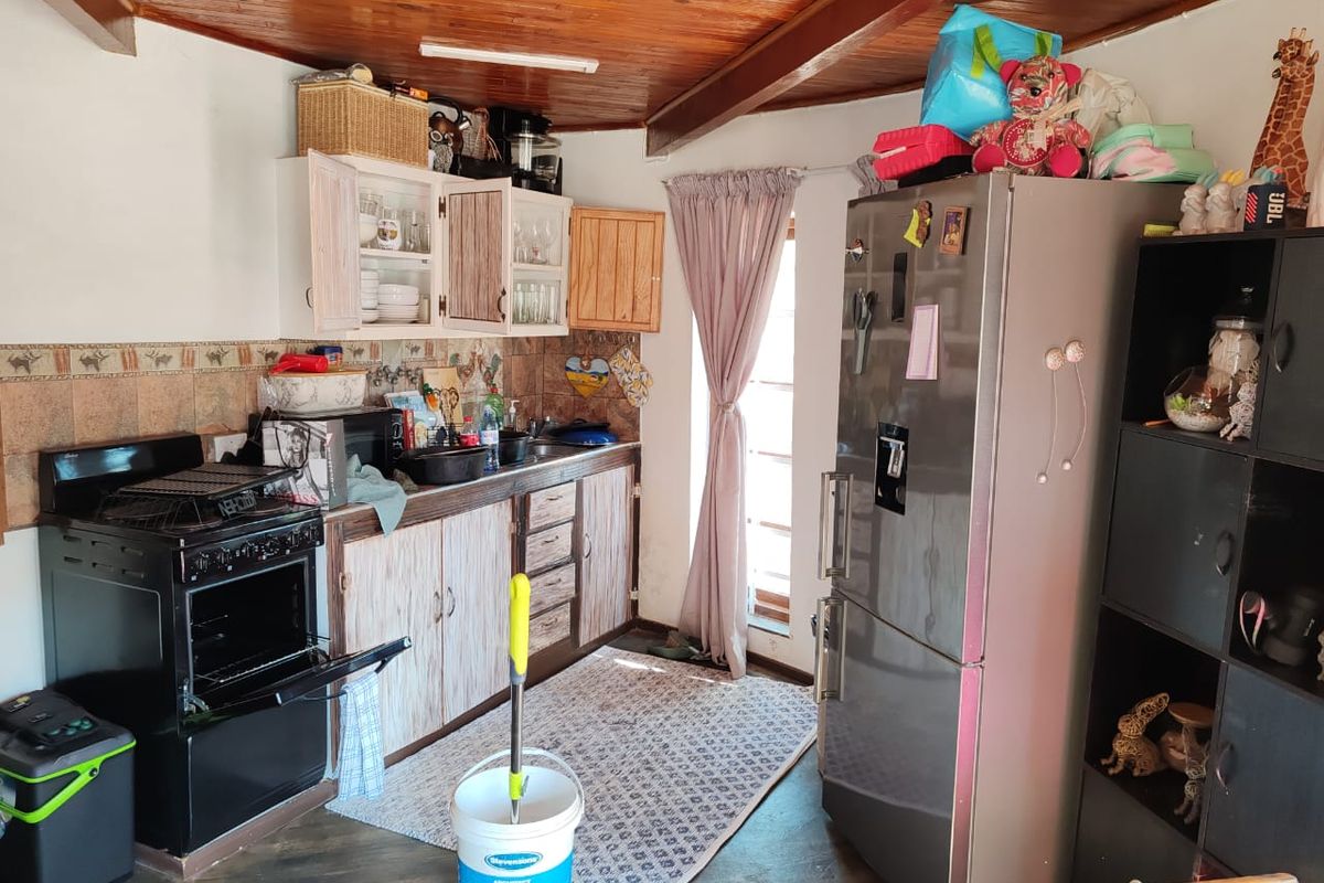 A compact kitchen featuring timber ceilings, tiled backsplash, and functional cabinetry. The space would benefit from modern updates to finishes and fixtures.