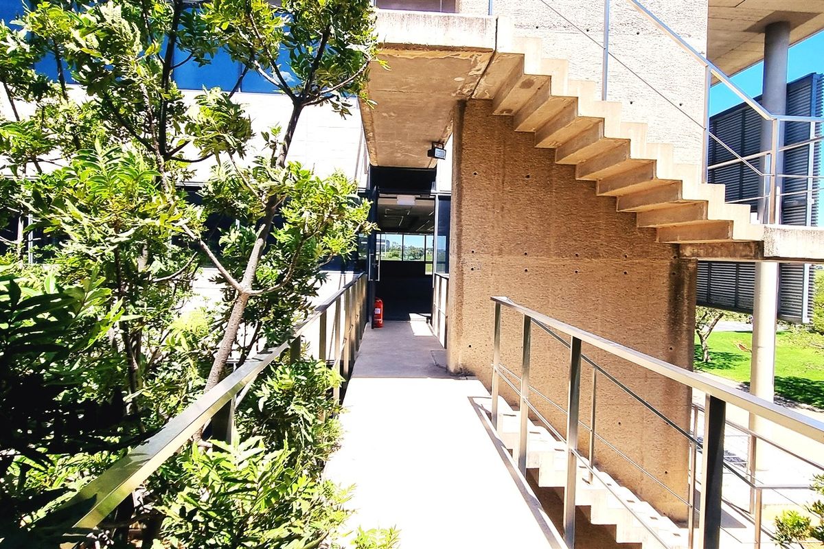 Exterior walkway featuring concrete construction, stainless steel railings, and an external staircase leading to the office building entrance.