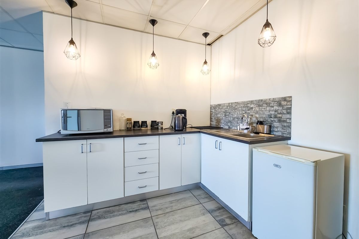 A compact office kitchenette featuring white cabinetry, a dark countertop, a stainless steel sink, and a tiled backsplash.