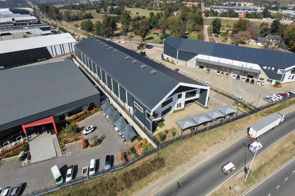 Aerial view of a modern industrial warehouse complex featuring large metal-clad buildings, paved parking areas with shade ports, and secure perimeter fencing.
