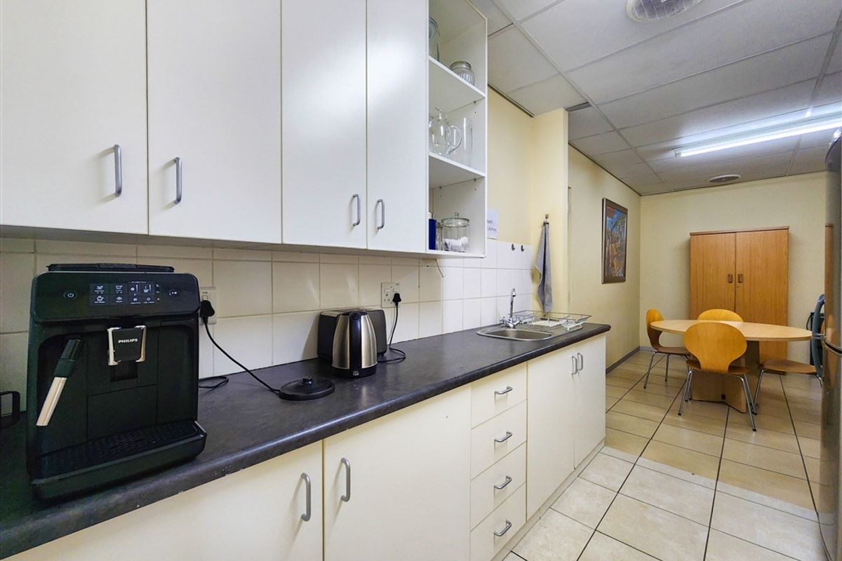Office kitchenette featuring laminate countertops, built-in cabinetry, stainless steel sink, and tiled flooring, with an adjacent small dining or breakout area.